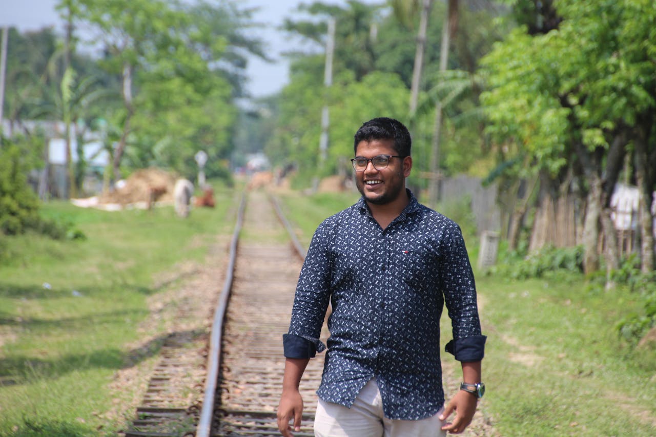 home-hero Smiling man casually walking on railway tracks surrounded by lush greenery in Jamalpur, Bangladesh.